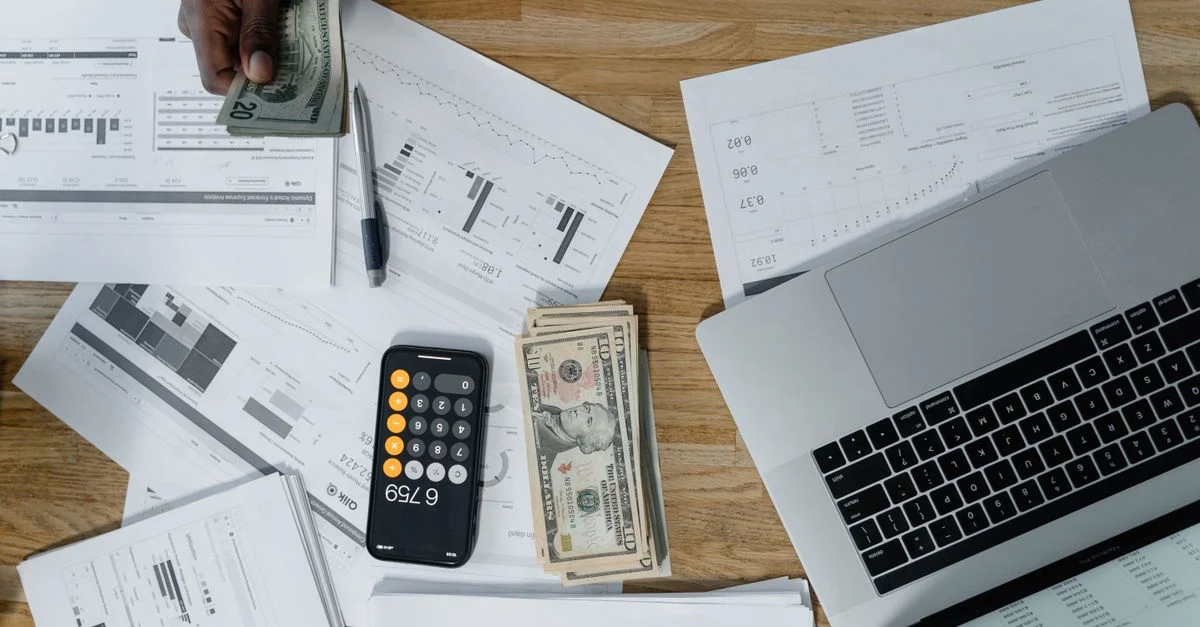 Vue de dessus d'un espace de travail animé avec de l'argent, des documents financiers et un ordinateur portable.