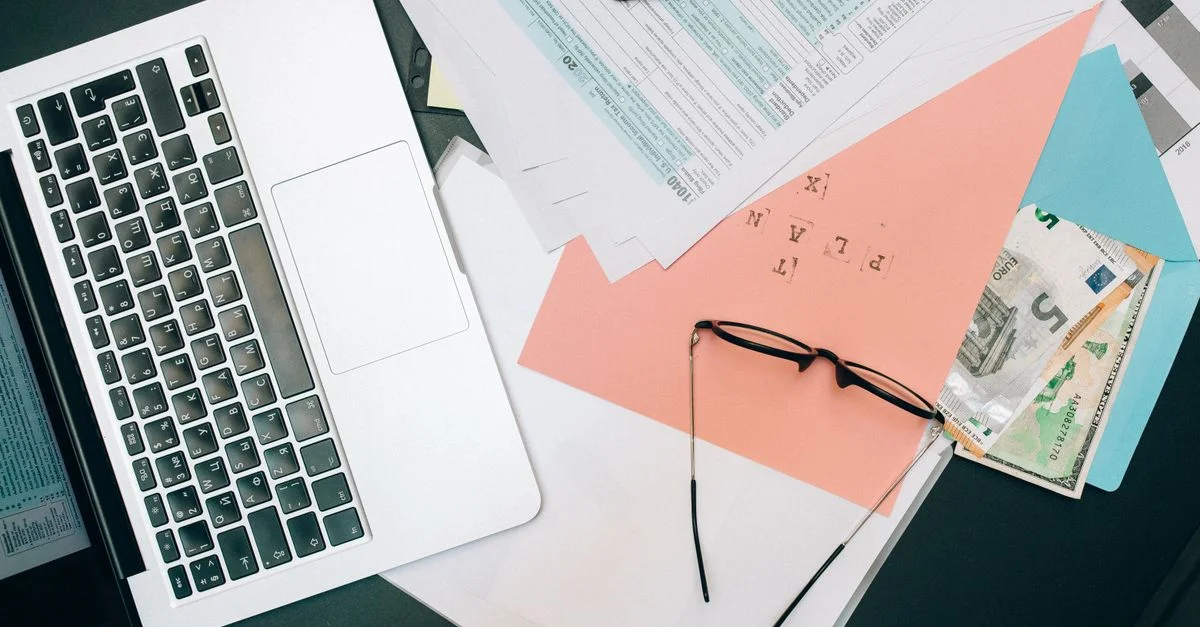 Un espace de travail soigné avec un ordinateur portable, des documents et des lunettes pour la productivité.