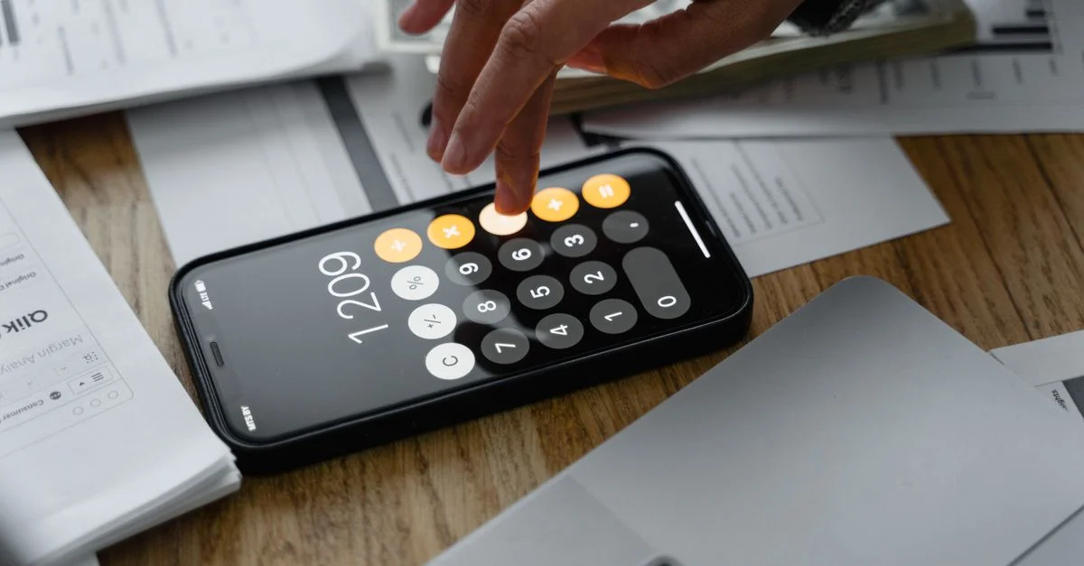 Gros plan sur une personne utilisant une calculatrice smartphone sur une table avec des documents pour des calculs financiers.