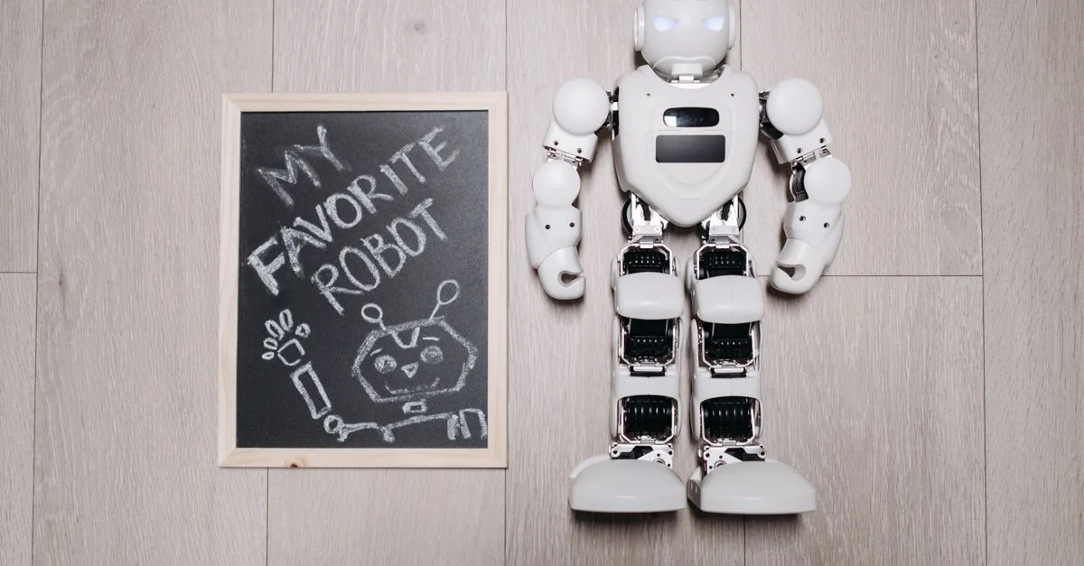 Vue en plongée d'un jouet robot à côté d'un dessin sur tableau noir, sur un sol en bois clair.